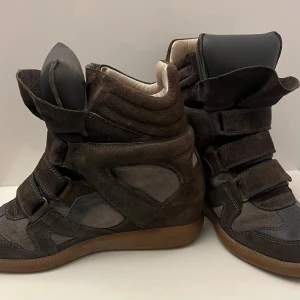 Bruna sneakers från Isabel Marant - Snygga bruna sneakers från Isabel Marant med hög design och kardborreband. Skorna har en robust gummisula och är tillverkade i mocka och skinn. Perfekta för en trendig look. Kontakta om det förekommer frågor !❤️