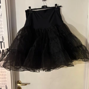 Svart tyllkjol - Snygg svart underkjol tyllkjol med voluminöst lager av tyll som ger en dramatisk look. Perfekt för att skapa en unik stil. Kjolen har en hög midja och är kort i längden.