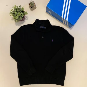 Stickad polo Ralph Lauren tröja - Säljer en stilren svart tröja från Polo Ralph Lauren i storlek L. Tröjan har långa ärmar och en klassisk krage med knappar. Perfekt för både vardag och festliga tillfällen. Den är i mycket bra skick och redo för en ny ägare! Skriv vid minsta fråga eller fundering💯👍