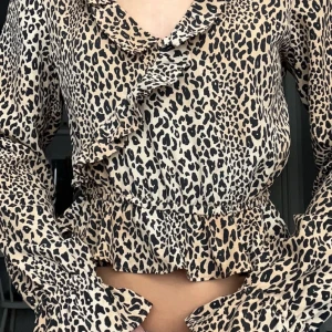 Leopardmönstrad blus med volangdetaljer - Snygg leopardmönstrad blus i storlek 32/xs/xxs med volangdetaljer och långa ärmar. Skicket på blusen är bra då ja inte fått användning. Perfekt för att ge en trendig touch till din outfit. 