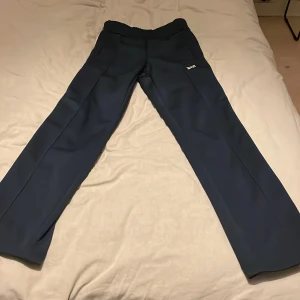 Mörkblå byxor med vita ränder - Snygga mörkblå byxor med vita ränder längs sidorna och dragkedja vid bensluten. Perfekta för en sportig look. Byxorna har en liten vit logotyp på ena benet. De är äkta finns kvitto. Ny pris 6000/7000 kr hör av er vid funderingar 😃