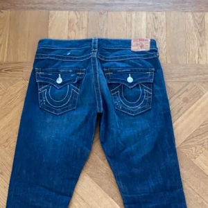 Blå jeans från True Religion - Snygga blå jeans från True Religion med ikoniska bakfickor och kontrastsömmar. De har en klassisk femficksdesign och en knappgylf. Perfekta för en avslappnad stil. Köpte på vinted men var försmå så därför jag säljer! Skriv vid frågor eller funderingar. Storlek 26. Öppen vid prisförslag!!