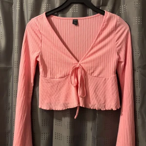 Rosa ribbad topp från Shein - Säljer en söt rosa ribbad topp från Shein med långa ärmar och v-ringning. Toppen är croppad och har en knytning framtill som ger en fin detalj. 