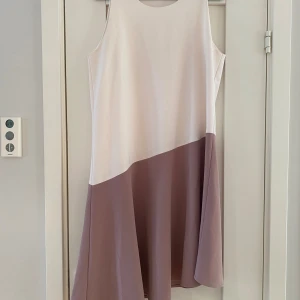 Plommonlila och beige klänning från Kiomi i strl 40 - Plommonlila och beige klänning från Kiomi i strl 40.  Sparsamt använd men tyvärr finns det en ljus fläck efter deodorant på framsidan i övrigt i bra begagnat skick.  Mått Över bröstet: ca 49 cm Längd från axeln och ner: ca 97 cm (kortaste delen)