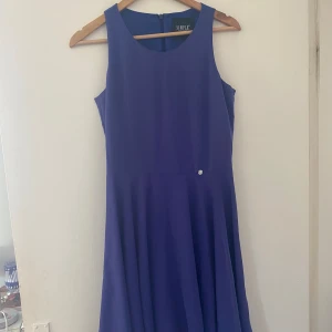 Blå ärmlös klänning från Simple - Säljer en elegant blå klänning från Simple. Den är ärmlös och har en rund halsringning. Klänningen är i ett lätt och flödande material som ger en fin passform. Perfekt för sommarens fester eller andra speciella tillfällen. Den har en dragkedja i ryggen för enkel på- och avklädning. Oanvänd. 