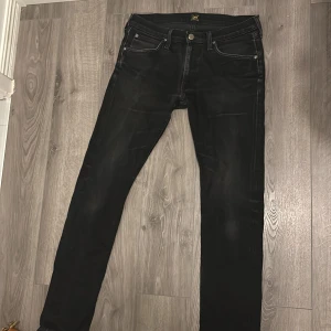 Svarta jeans från Lee - Säljer ett par svarta jeans från Lee i modellen LUKE. De är i bra skick och har en dragkedja och knapp framtill. Jeansen har en klassisk femficksdesign och är tillverkade i ett slitstarkt material. Perfekta för både vardag och fest! Dm för fler funderingar.
