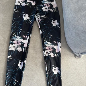 Blommiga leggings - Säljer ett par snygga leggings/träningsbyxor med blommigt mönster. De är svarta/marinblå med vita och rosa blommor samt gröna blad. Perfekta för både träning och vardagsbruk. De är i bra skick och väldigt bekväma att ha på sig. 