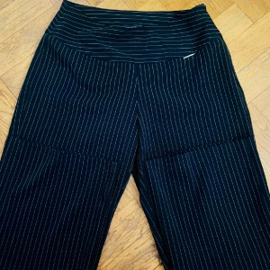 Svarta randiga byxor - Säljer ett par svarta byxor med vita ränder. Byxorna har en hög midja och en rak passform med dragkedja på sidan. Perfekta för vardag 