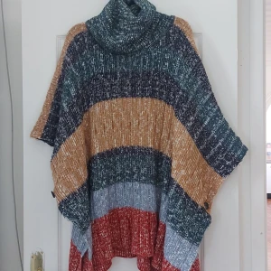 Flerfärgad stickad poncho - Säljer en supermysig stickad poncho i flera färger. Den har en stor polokrage och är perfekt för höst och vinter. Färgerna är en mix av blått, grönt, beige och rött. Den är M/L  och har knappar på sidorna. Perfekt att slänga på sig över en tröja för extra värme och stil!