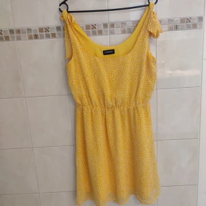 Gul klänning  - Gul klänning med vita prickar och rosetter på axlarna. Material: 100% polyester 