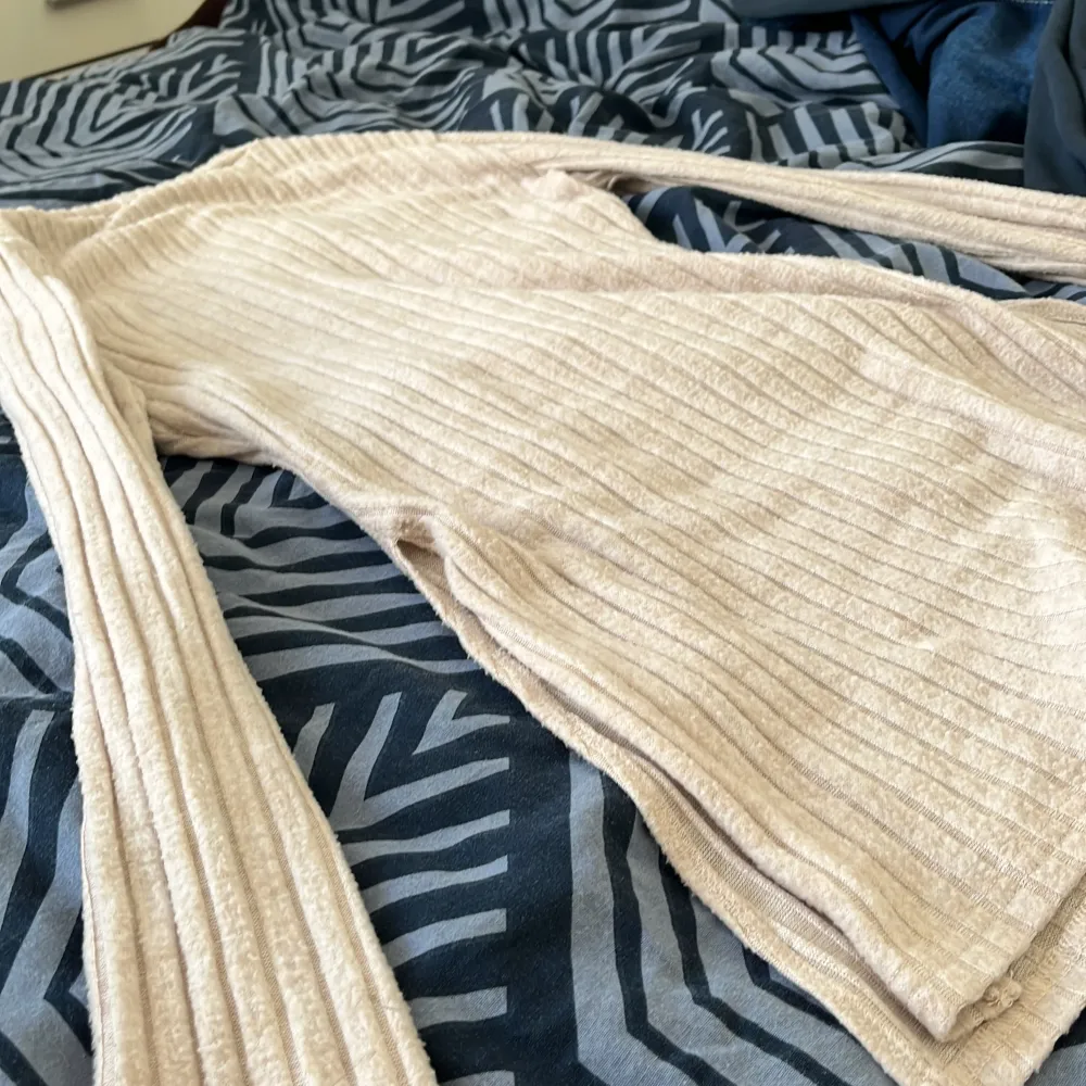 Säljer en superfin beige ribbad byxdress. Den är gjord av ett mjukt och stretchigt material som känns skönt mot huden. Byxdressen har långa ärmar och vida byxben, vilket ger en avslappnad och stilren look. Perfekt för både vardag och fest!. Övrigt.