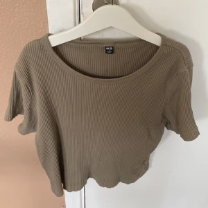 Beige ribbad topp från Uniqlo - Säljer en snygg militär-grön ribbad topp från Uniqlo. Den är kortärmad och har en croppad passform som är perfekt för sommaren. Toppen är tillverkad i ett mjukt och bekvämt material som känns skönt mot huden. Perfekt för både vardag och fest! köparen betalar för frakt!