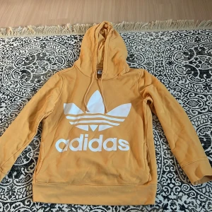 Hoodie adidas - Gul/ljusorange hoodie från adidas med ficka vid magen. Inga tydligare tecken på använding utan den är i mkt bra skick! Strl M