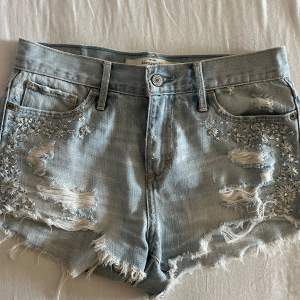 Säljer ett par snygga lågmidjade jeansshorts från Abercrombie & Fitch i storlek W26/S. De har en cool distressed look med slitningar och fransar längs kanterna. Shortsen är dekorerade med broderade blommor och små pärlor på framsidan, köpta här på plick men tyvärr lite för små i midjan så säljer därför vidare! 🥰💕💕 kan gå ner i pris vid snabb affär🥰