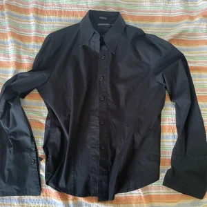 Svart skjorta från Jacqueline - Säljer en stilren svart skjorta från Jacqueline i storlek L. Skjortan har långa utsvängda ärmar och knappar längs hela framsidan. Perfekt för både formella och avslappnade tillfällen. Materialet känns bekvämt och hållbart. Passar bra till både jeans och kostymbyxor.