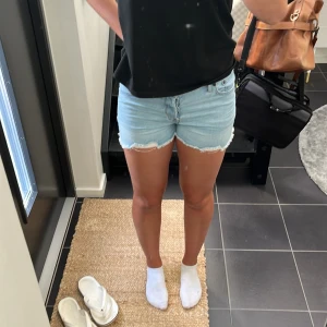 Ljusblå jeansshorts - Säljer ett par ljusblå jeansshorts med råa kanter. De är perfekta för sommaren och har en avslappnad, loose passform och är lowwaist. Shortsen har knappar framtill och är i nyskick. Perfekta för en dag på stranden eller en somrig utflykt!