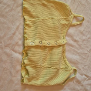 Gul ribbad croppad topp - Säljer en superfin gul ribbad topp som är croppad och har knappar framtill. Toppen är ärmlös och har smala axelband. Perfekt för sommaren eller en festlig kväll! 🌞