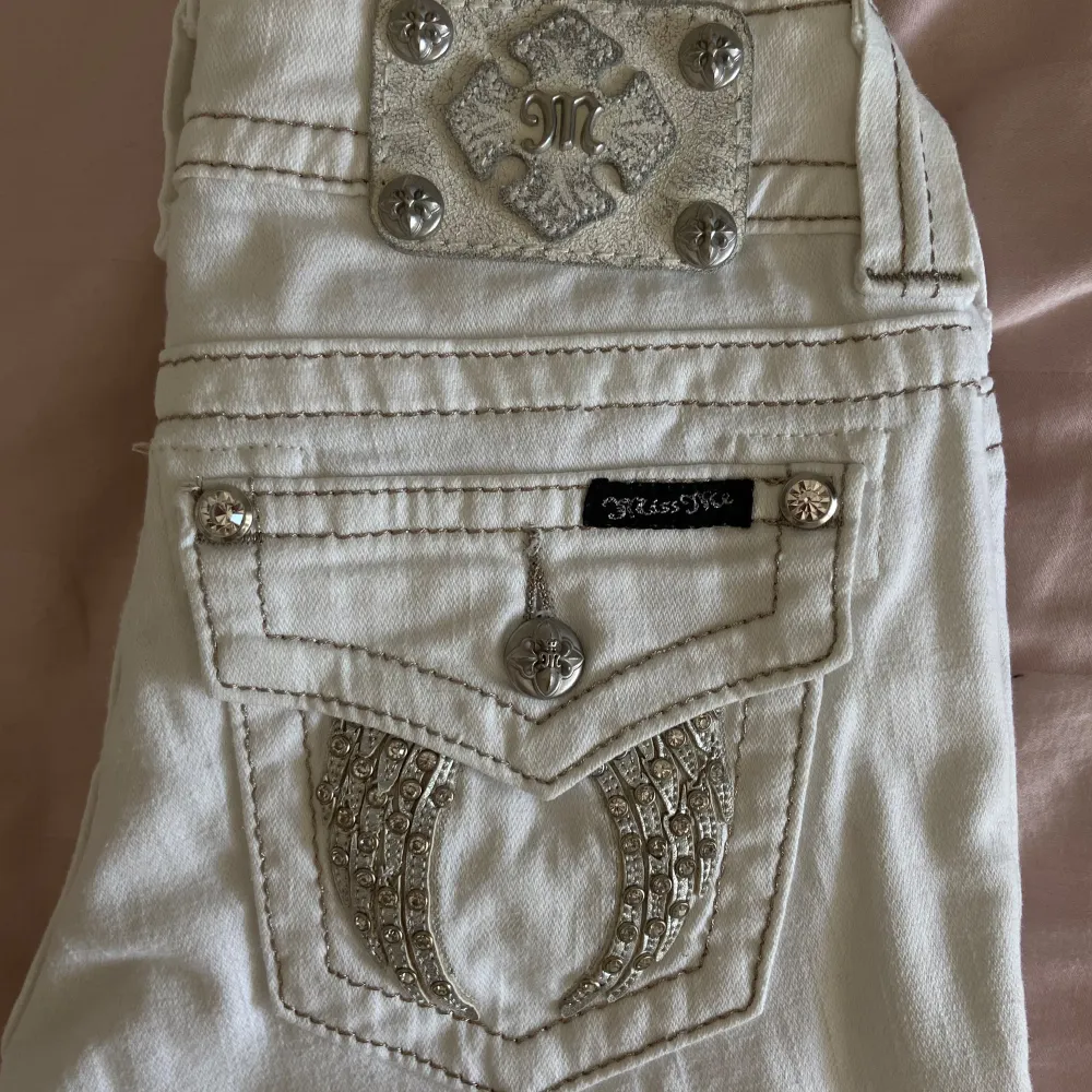 Säljer ett par snygga vita jeans från Miss Me i storlek 25. De är lågmidjade och har en tight passform som verkligen framhäver figuren. Jeansen har coola detaljer med knappar och broderier på bakfickorna. Perfekta för både vardag och fest!. Jeans & Byxor.