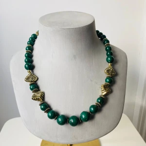 Grönt halsband med gulddetaljer - Säljer ett supercoolt grönt halsband med stora pärlor och snygga guldfärgade detaljer. Plast. Det har en unik design med guldfärgade fjärilar som ger en extra touch av elegans. Perfekt för att piffa upp vilken outfit som helst! 💚✨