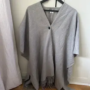 Jättefin grå stickad poncho med fransar nedtill. Använd vid max 5 tillfällen. Tror den är köpt på Cubus. One Size. Så fin framåt nu till vårens   Material: tror det är 100% polyester.  Djur- och rökfritt hem.