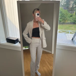 Beige kavaj och byxor - Säljer en snygg beige kavaj med matchande byxor. Kavajen har en klassisk design med knappar framtill och fickor. Byxorna är raka och har en slits vid anklarna. Perfekt för både vardag och fest! detta är alltså ett set