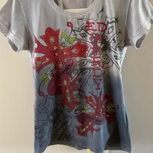 Läs info 💕💕Säljer en grå Ed Hardy t-shirt med coolt tryck i rött och grönt.  Den har ett stort korsmotiv med texten 'Ed Hardy' på framsidan och loggan på baksidan. Har defekter!💕Står storlek xl men känns som M