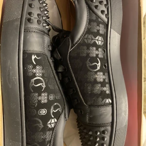 Svarta sneakers från Christian Louboutin - Säljer ett par svarta sneakers från Christian Louboutin i mycket bra skick. Skorna har en cool design med nitar och mönster på sidorna. Den ikoniska röda sulan ger en lyxig touch. Perfekta för att lyfta vilken outfit som helst! Den fanns att hämta i Eskilstuna annars kan jag skicka den med paket! 🖤