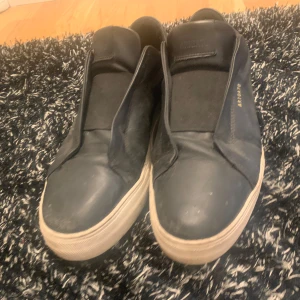 Svarta sneakers från Axel Arigato - Säljer ett par svarta sneakers från Axel Arigato i bra skick. De har en stilren design med en vit sula och är perfekta för vardagsbruk. Skorna är gjorda i skinn och har en diskret logga på sidan. Passar perfekt till både jeans och mer uppklädda outfits. Storlek 43