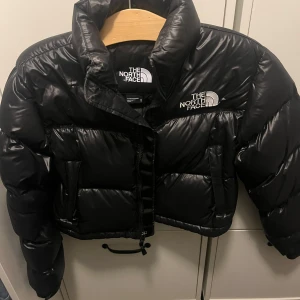 Svart pufferjacka från The North Face - Säljer en snygg och varm svart pufferjacka från The North Face i storlek XS. Jackan har en hög krage och dragkedja framtill. Perfekt för kalla vinterdagar och har en stilren look. Den är i mycket bra skick och redo för nya äventyr! 🖤