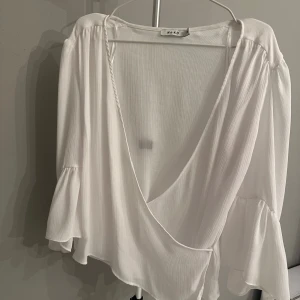 Vit omlottopp från NA-KD - Säljer en superfin vit omlottopp från NA-KD i storlek 38. Toppen har långa ärmar med volangdetaljer och en djup v-ringning. Perfekt för både vardag och fest! ✨