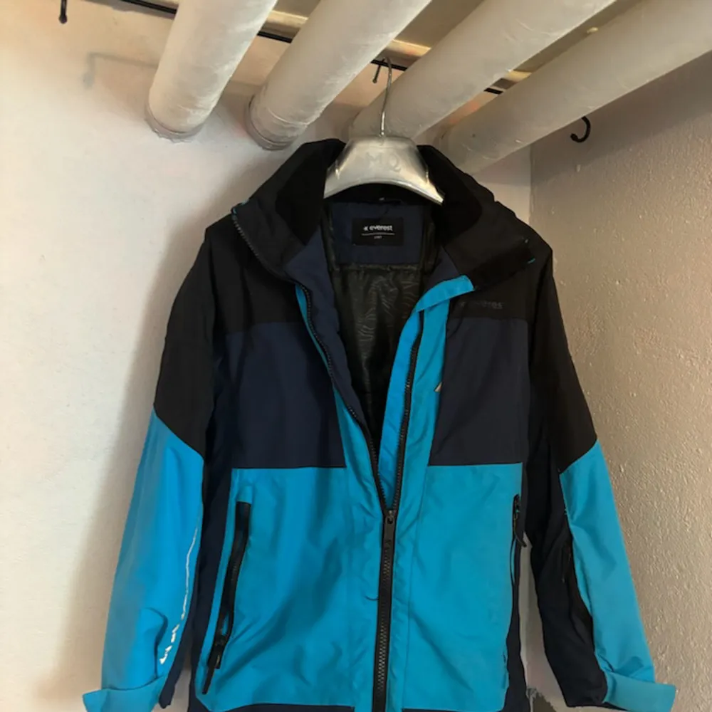 Säljer en snygg blå och svart vinterjacka från Everest. Jackan har en dragkedja framtill och långa ärmar. Perfekt för kalla vinterdagar med sin varma och skyddande design. Den har en sportig look och är i mycket bra skick.. Jackor.