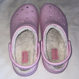 Rosa Crocs med foder - Supermysiga rosa Crocs med fluffigt foder för extra komfort. Perfekta för att hålla fötterna varma och sköna under kyliga dagar. De har den klassiska Crocs-designen med hål för ventilation och en justerbar hälrem för bättre passform. Användbara både inomhus och utomhus!