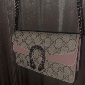 liten väska - Säljer en snygg axelväska med det klassiska monogrammönstret. Väskan har en stilren design med en kedjerem och en unik detalj på framsidan. Perfekt för både vardag och fest!