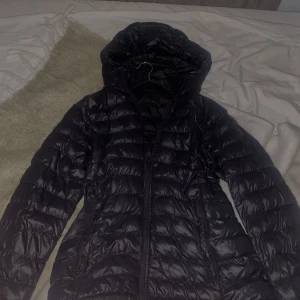 Svart everest pufferjacka med huva - Säljer en svart pufferjacka i mycket bra skick. Den har en praktisk huva och dragkedja framtill. Perfekt för kyliga höst- och vinterdagar. Jackan är lätt och bekväm, vilket gör den idealisk för vardagsbruk.