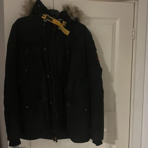 Svart vinterjacka från Parajumpers - Säljer en svart Parajumpers vinterjacka i mycket bra skick. Jackan har en fluffig pälsdetalj på huvan och flera praktiska fickor. Den är perfekt för kalla vinterdagar och har en snygg gul detalj vid halsen. Passar både till vardags och mer äventyrliga aktiviteter. Pris går att diskutera, ny pris på denna jacka ligger runt 12-13 tusen 
