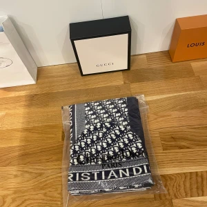 Mössa och halsduk från Christian Dior - Säljer en snygg mössa och halsduk från Christian Dior i marinblått och vitt. Setet har ett klassiskt mönster med märkets logga tydligt broderad. Perfekt för att hålla stilen i vinterkylan. Både mössan och halsduken är i nytt skick och kommer i originalförpackning.