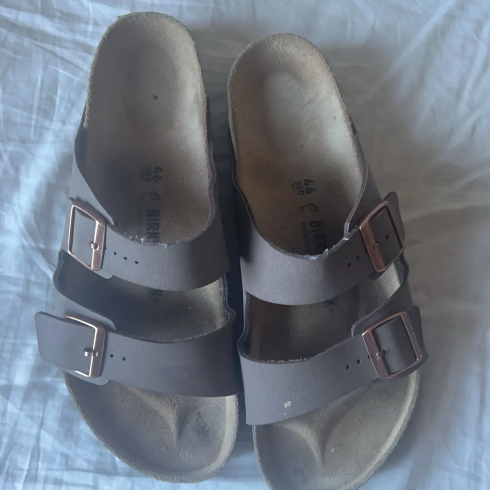 Säljer ett par klassiska Birkenstock sandaler i brunt läder. De har två justerbara remmar med metallspännen och en bekväm fotbädd. Perfekta för sommaren och ger bra stöd för fötterna. Använda men i bra skick.. Skor.