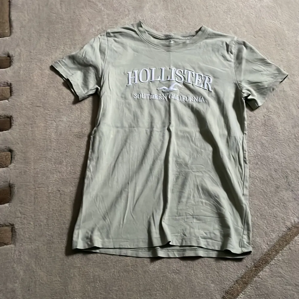 Säljer en snygg grön t-shirt från Hollister med broderi på framsidan. Den är i bra skick och perfekt för en avslappnad stil. Kortärmad och gjord i mjukt material.. T-shirts.