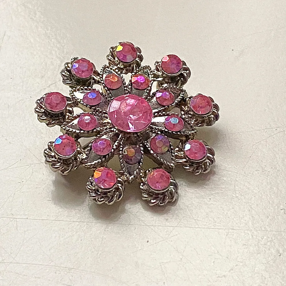 Säljer en superfin vintage brosch i form av en blomma med gnistrande rosa stenar. Den har en silverfärgad bas och är perfekt för att piffa upp vilken outfit som helst. Broschen är cirka 4 cm i diameter och har en säkerhetsnål på baksidan för enkel fastsättning. Perfekt för fest eller som en unik accessoar till vardags! 🌸. Accessoarer.