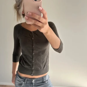 Mörkgrå kofta med knappar - Säljer en stilren mörkgrå kofta med knappar framtill. Den har en tight passform och trekvartsärmar, perfekt för både vardag och fest. Koftan är i bra skick och passar utmärkt till jeans eller kjol. Perfekt för höst och vår!