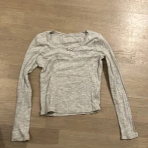 Grå långärmad topp med spetsdetaljer - Säljer en söt grå långärmad topp med spetsdetaljer runt halsringningen. Perfekt för både vardag och lite finare tillfällen. Toppen är i bra skick och har en liten rosett framtill. Passar perfekt till jeans eller kjol! Från HM