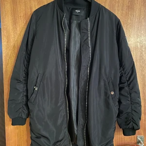 Svart bomberjacka - Säljer en svart bomberjacka i bra skick. Den har en dragkedja framtill och långa ärmar. Perfekt för höst och vår, med en klassisk och stilren look. Jackan har ribbade muddar vid ärmslut och nederkant för extra komfort.