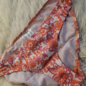 Mönstrad bikiniunderdel i orange och rosa - Säljer en superfin bikiniunderdel med ett färgglatt mönster i orange och rosa. Perfekt för sommarens stranddagar! Materialet känns mjukt och bekvämt mot huden. Passar perfekt för både bad och soliga dagar vid poolen. 🏖️