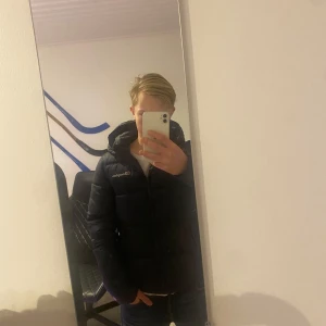 Marinblå pufferjacka från Champion - Väldigt snygg vinterjacka i nyskick. Ändå är att det är ett pytte litet hål som är lagad som syns på bilden, annars väldigt bra skick. Tveka inte att höra av er vid funderingar.