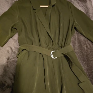 Olivgrön klänning från Weekday - Säljer en stilren olivgrön Jumpsuit från Weekday i storlek 34(stor i storlek)Jumpsuot har trekvartsärmar och ett bälte i midjan för en snygg passform. Perfekt för både vardag och festliga tillfällen. Materialet känns mjukt och bekvämt.
