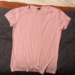 Rosa t-shirt - Säljer en enkel och stilren rosa t-shirt i mjukt material. Perfekt för vardagsbruk eller sommarens varma dagar. T-shirten har en normal passform och korta ärmar. Ett måste i garderoben för en avslappnad look!