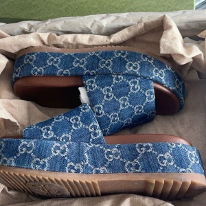 Gucci sandaler  - Säljer ett par snygga blå sandaler från Gucci i jeansmaterial. De har en bekväm platåsula och är perfekta för sommaren. Passar både till vardags och festliga tillfällen. Skorna är i mycket bra skick, har låda samt bagsen till skorna. De är i storlek 36 men skulle säga att de passar 37