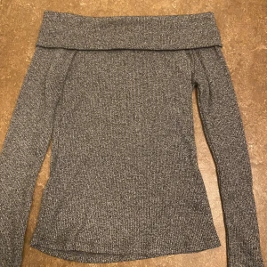 Grå offshoulder tröja - Säljer en snygg grå offshoulder tröja i ribbat material. Perfekt för både vardag och fest! Tröjan har långa ärmar och en bekväm passform som sitter bra på kroppen. Den är stilren och lätt att matcha med olika outfits.  