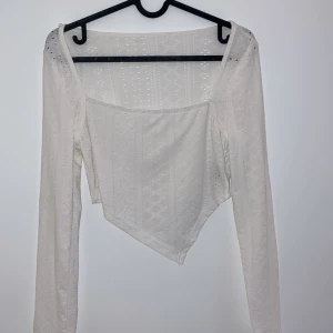 Vit asymmetrisk topp - Säljer en superfin vit topp med asymmetrisk design och långa ärmar. Toppen har ett subtilt mönster och är perfekt för både vardag och fest. Den är i mycket bra skick och passar perfekt till jeans eller kjol.