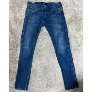 Blå jeans från Replay - Säljer ett par snygga blå jeans från Replay i mycket bra skick. De har en slim passform och är perfekta för både vardag och fest. Jeansen har en klassisk femficksdesign och en dragkedjegylf. De är tillverkade i ett stretchigt material som ger en bekväm känsla hela dagen. Den har en mindre skada i grenen som är lätt att laga (syns i sista bilden). Färg: 009 MEDIUM BLUE Storlek: 32"32